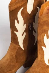 Bota estilo texana de gamuza color marrón, con diseño de apliques en forma de llamas en color crema y taco de madera.