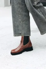 Bota tipo Chelsea de cuero color marrón, con paneles laterales elásticos en color negro y suela track robusta de goma negra.