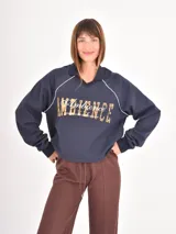 Buzo azul oscuro de corte holgado con cuello polo y escote en V. Presenta mangas largas con costuras raglán en color blanco y un estampado frontal con la palabra Ambience y el texto United Nation League en tonos dorados.