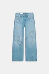 Jeans de denim celeste lavado, corte boyfriend ancho, tiro medio, con roturas y apliques/bordados en forma de corazón en diferentes partes de las piernas.