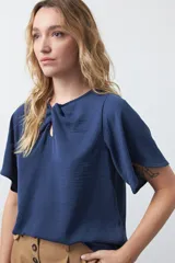 Top negro de manga corta con detalle de nudo en el escote y abertura tipo gota. Presenta una silueta relajada y textura sutil en la tela.