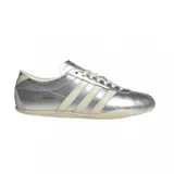 Championes Adidas modelo Tokyo, con diseño de perfil bajo en color plateado metalizado. Presenta las icónicas tres tiras laterales y suela en tono crema, con el logo de la marca y el nombre del modelo grabados en el lateral.