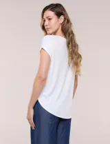 Remera blanca de punto acanalado con escote redondo adornado con tachas metálicas en el cuello y hombros, mangas cortas japonesas y ruedo curvo.