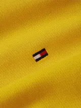 Chomba Tommy Hilfiger amarilla de corte slim, con cuello y puños acanalados, cartera de dos botones y logo de bandera bordado en el pecho.