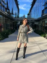 Vestido camisero corto color verde con textura arrugada, manga larga, cuello camisero, cierre frontal con botones, cinturón negro con hebilla dorada y bolsillos con solapa en el pecho.