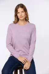 Buzo tejido en hilo de algodón color beige, con cuello redondo y manga larga. Presenta un corte clásico y un pequeño detalle metálico en la parte inferior izquierda.