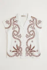 Camisa blanca de manga corta con cuello solapa, cierre frontal de botones y diseño bordado en hilo azul marino con motivos florales y vegetales.