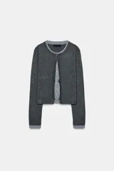 Chaqueta de punto con diseño de doble capa, cuello redondo y manga larga. Presenta una capa exterior gris oscuro y una capa interior gris claro con estampado de rombos, ambas con cierre frontal de botones.