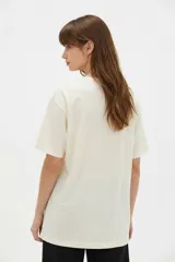 Remera de algodón color beige con estampado frontal de un corazón rosado que contiene un moño. Tiene cuello redondo y mangas cortas.