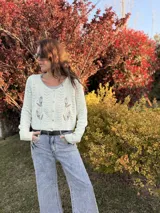 Saco tejido de punto color blanco marfil, con cuello redondo, cierre frontal con botones y bordados florales en el frente.