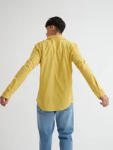 Camisa manga larga amarilla de algodón con bolsillo en el pecho, botones de pasta, logo bordado en el ruedo y etiqueta de marca en la tapeta de botones.