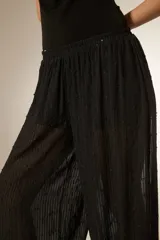 Pantalón tipo babucha de color negro, confeccionado en tela semitransparente con textura de rayas verticales y pequeños detalles en relieve. Presenta una cintura elástica cómoda y un corte holgado que se ajusta ligeramente en los tobillos.