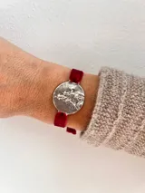 Pulsera plateada con dije circular con grabado y banda de terciopelo elástico color rojo.