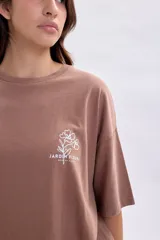 Remera de manga corta con corte oversize, color marrón, con estampa lineal blanca en la espalda que representa un florero con flores y el texto Jardin Fleuri.