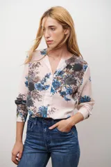 Camisa de manga larga con cuello redondo y cierre frontal de botones. Presenta un estampado floral en tonos azules y marrones sobre una base de color rosado claro.