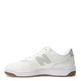 Championes urbanos New Balance de cuero sintético color blanco con detalles en verde claro y suela de goma color caramelo.