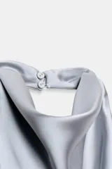 Top blanco satinado con cuello halter y escote fluido. Cierre en la espalda con botones.