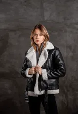 Campera tipo gamulán de eco cuero negro con interior y solapas de corderito sintético en color crudo. Presenta cierre frontal, bolsillos laterales con cierre y cinturón ajustable en la cintura.