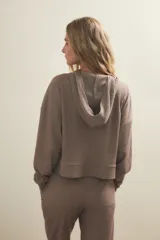 Buzo con capucha de tejido acanalado, corte holgado y mangas largas con puños. Presenta un diseño minimalista con aberturas laterales en el ruedo.