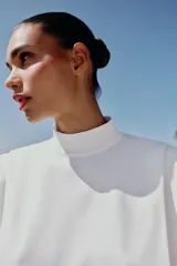 Top de punto color marrón oscuro, con cuello subido, manga sisa con hombreras, pliegues y espalda descubierta con cierre trasero de botones.