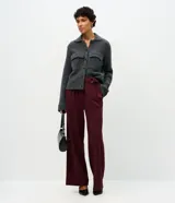 Pantalón de corte wide leg confeccionado en crepé color bordó, con cintura alta, cierre frontal con cremallera y detalle de hebilla ajustable en la cintura.