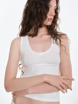 Musculosa de punto pointelle color gris melange, con escote redondo, detalle de picot en los bordes y una pequeña moña decorativa en el centro del pecho.