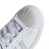 Championes adidas modelo Superstar, de diseño clásico con exterior de cuero blanco, puntera de goma reforzada y las icónicas tres tiras laterales en tono gris claro.