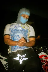 Camiseta deportiva blanca con cuello en V negro, inspirada en azulejos portugueses. Presenta un gran estampado central de la Virgen María con el niño Jesús en un marco ovalado azul y blanco, rodeado de motivos florales en azul y amarillo.