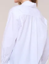 Camisa blanca de corte holgado, marca Magaschoni, con cuello camisero, mangas largas con puños anchos, bolsillo en el pecho y ruedo curvo.