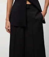 Pantalón pantacourt negro de sastre, con cintura alta, cierre interno discreto y pliegues delanteros sutiles.