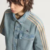 Camisa de jean de manga corta Adidas, confeccionada en 100% algodón, con diseño inspirado en la ropa de trabajo, cierre frontal con broches a presión, cuello camisero, un bolsillo en el pecho con solapa y las clásicas tres tiras de la marca en las mangas.