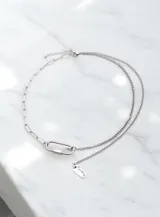 Collar de doble cadena de acero quirúrgico, compuesto por una cadena de eslabones alargados y una cadena fina. Presenta un mosquetón central como elemento decorativo y un dije rectangular con la palabra 'Destiny' grabada.
