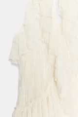 Top de encaje color blanco crudo, con cuello halter, escote en V profundo, volantes en los bordes y bajo asimétrico con lazada en el cuello.