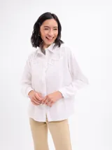 Camisa blanca de algodón, de manga larga, con detalle de tiras cruzadas en el canesú delantero y cierre frontal con botones.