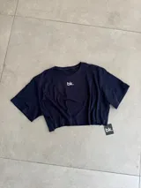 Remera de algodón azul marino, corte crop top y manga corta, con un pequeño logo blanco bordado en el pecho.