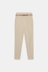 Pantalón tobillero de tiro medio en color beige, con diseño de corte recto y bolsillos delanteros. Incluye un cinturón fino de cuero sintético en tono marrón con hebilla metálica. Cierre frontal con cremallera, botón interior y gancho.