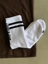 Medias blancas largas con dos rayas negras horizontales en la parte superior y logo vertical en el lateral.