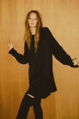 Vestido túnica negro de manga larga con cuello redondo ribeteado y abertura frontal con botón metálico. Presenta un tejido con textura arrugada y puños amplios con botón.