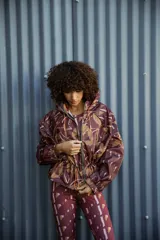 Campera impermeable con capucha y cierre frontal, con estampado de hojas en tonos marrones y ocres. Tiene bolsillos laterales ocultos y cordón ajustable en la cintura.