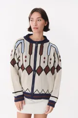 Campera tipo bomber tejida con diseño jacquard geométrico. Presenta cierre frontal completo, cuello redondo, puños y ruedo acanalados en contraste. Posee hombros caídos y un ajuste holgado.