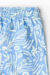 Short de baño celeste con estampado tropical en tonos claros, cintura elástica con cordón de ajuste y bolsillos laterales.