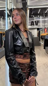 Campera corta tipo bolero de cuero sintético negro, con solapas anchas y cierre frontal con un botón. Presenta mangas largas con detalle de cordones cruzados a lo largo de todo el brazo.