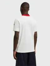 Polo de piqué de algodón color blanco, con cuello clásico a dos tonos (azul marino y rojo) y tapeta de dos botones.