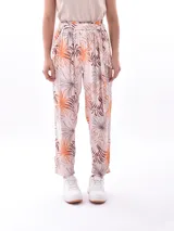 Pantalón babucha de tiro alto con cintura fruncida y lazo para ajustar. Estampado de hojas tropicales en tonos naranja y marrón sobre fondo blanco.