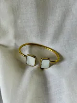 Pulsera rígida dorada con apliques cuadrados de nácar en los extremos.