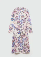 Vestido midi de algodón con estampado floral multicolor sobre fondo crudo. Presenta escote en pico, mangas largas con puños abotonados y un lazo decorativo en la cintura que crea un efecto drapeado, con una abertura frontal.