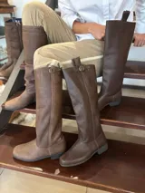 Bota alta de cuero marrón, con suela de goma y tira decorativa con hebilla metálica en la parte superior de la caña.