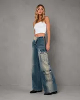 Pantalón cargo de jean azul con efecto gastado, tiro ajustable que permite usarlo alto o bajo mediante un cierre lateral, bolsillos cargo grandes en los laterales y diseño de pierna ancha.