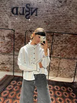 Camisa de corte clásico con estampado de rayas verticales en tonos celestes y marrones. Presenta volados delicados en el frente y en el cuello, cierre frontal con botones y mangas largas con puños ajustados.