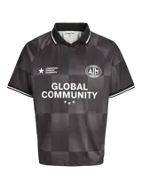 Camiseta de fútbol Jack & Jones Core, de corte holgado, con cuello polo y mangas cortas. Presenta un diseño de cuadros en tonos grises y negros, con estampados gráficos frontales que incluyen el texto 'Global Community' y logos deportivos.